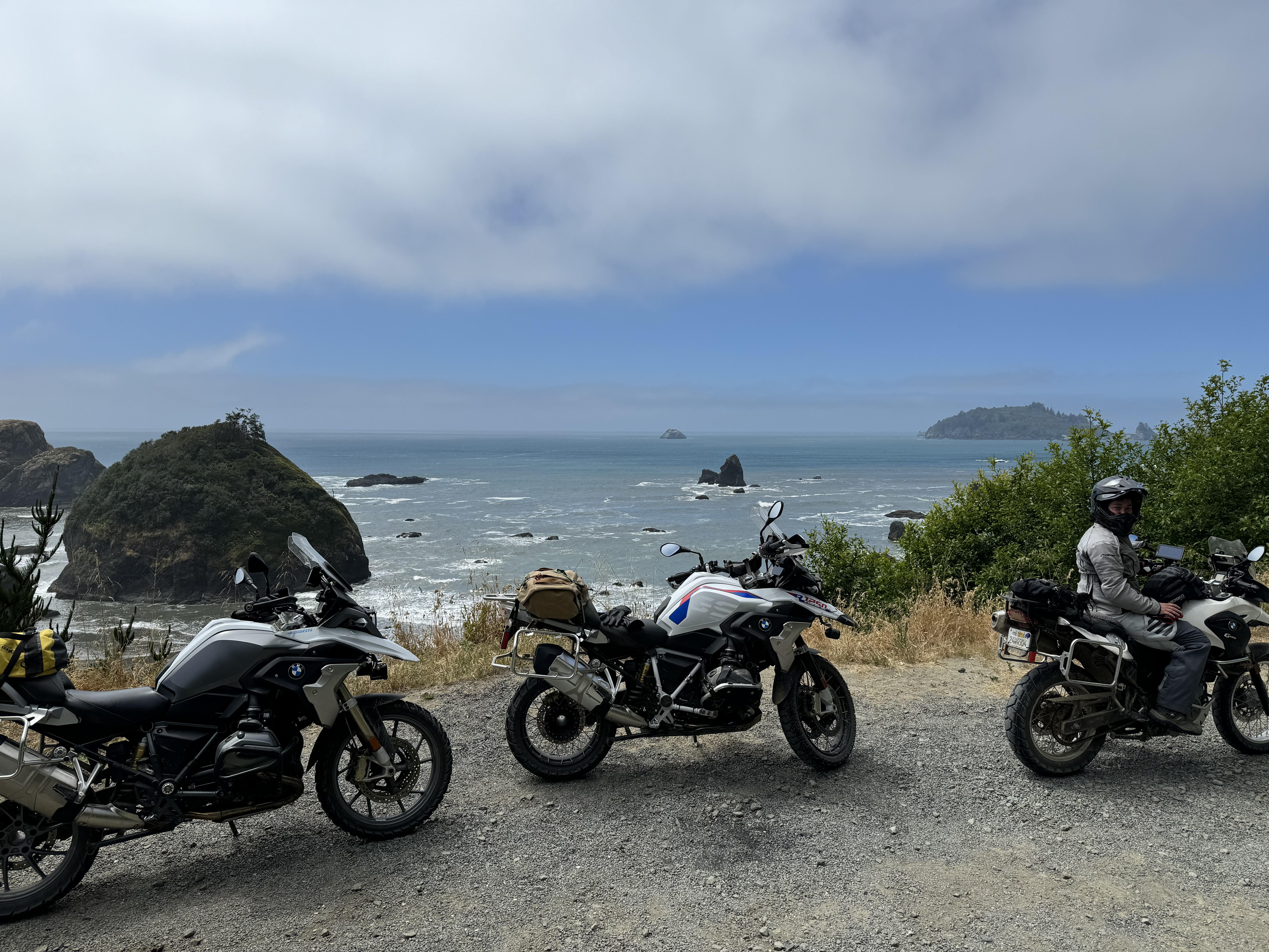 Three BMW GS adventure motorcycles overlooking a dramatic rocky rugged coastline and ocean in Northern California