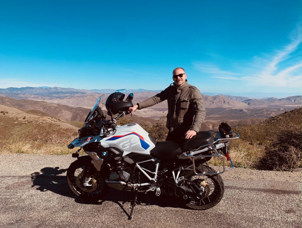 Motorcycle rider stands with BMW 1250GS Rallye overlooking mountains in the distance